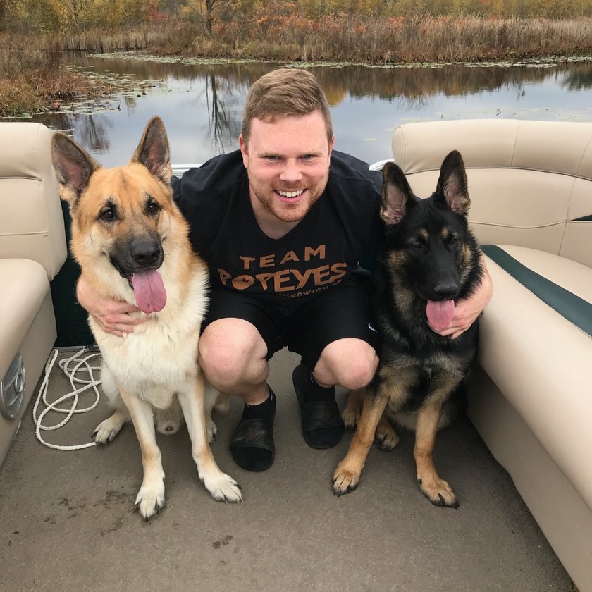 A person sitting between a tan and a black German Shepherd on a boat.